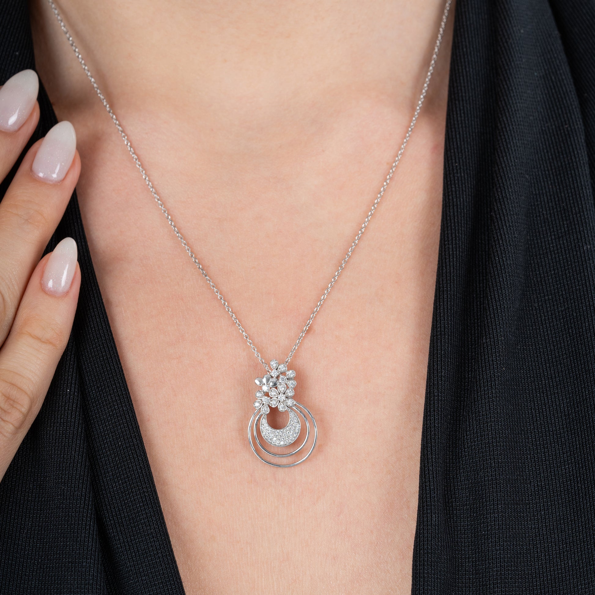 Silver necklace with a pendant on a person's neck against a black background