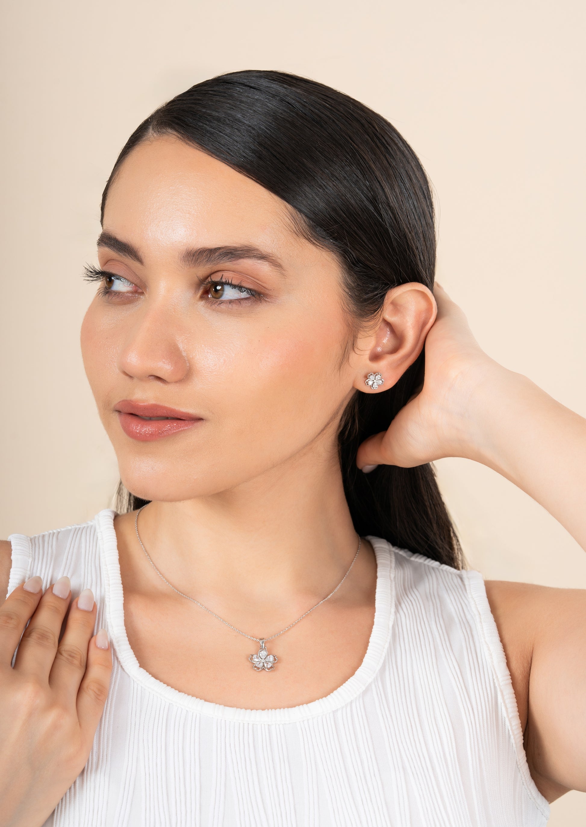 Woman wearing diamond earrings and necklace against a beige background