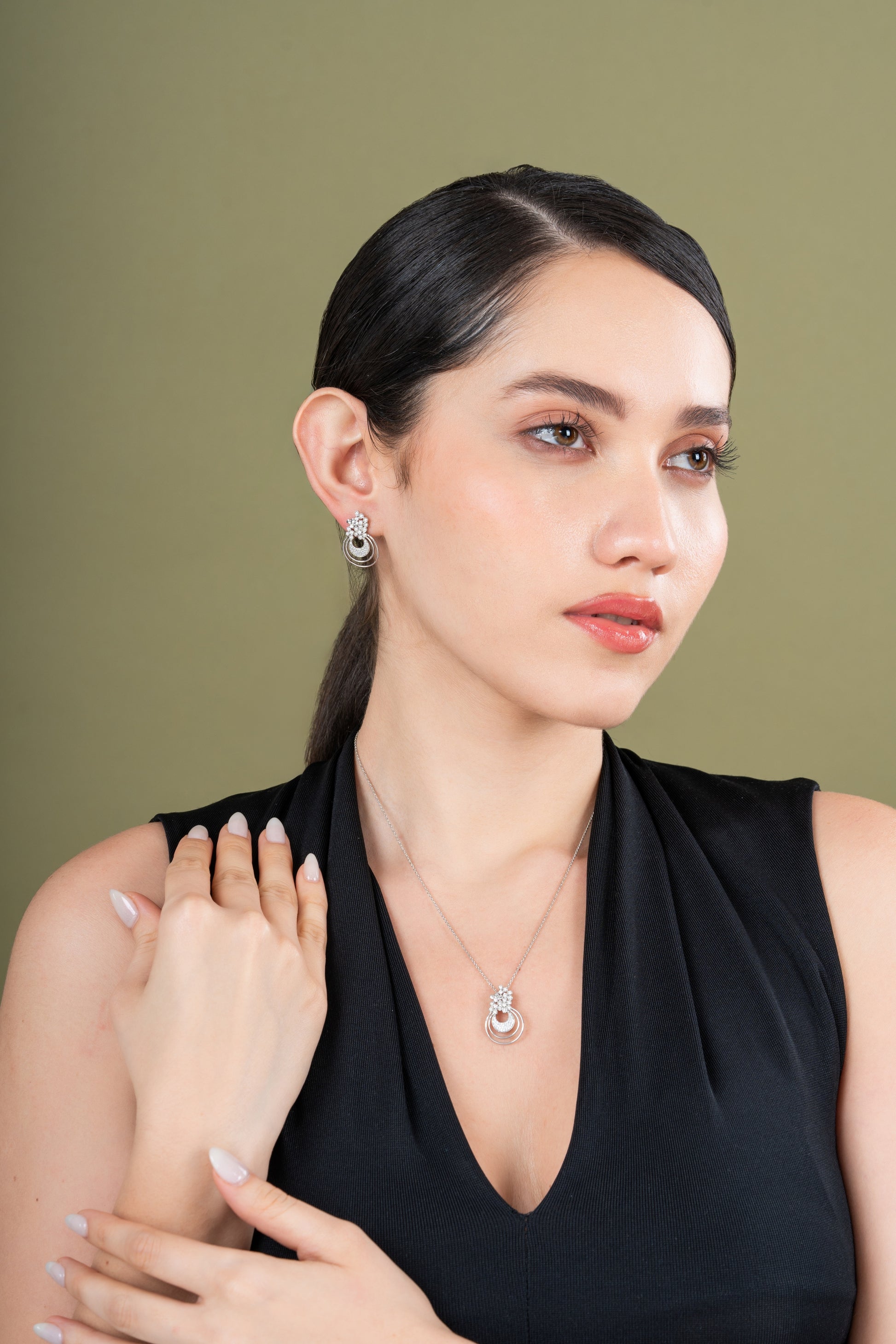 Woman wearing a black sleeveless top with jewelry against a green background